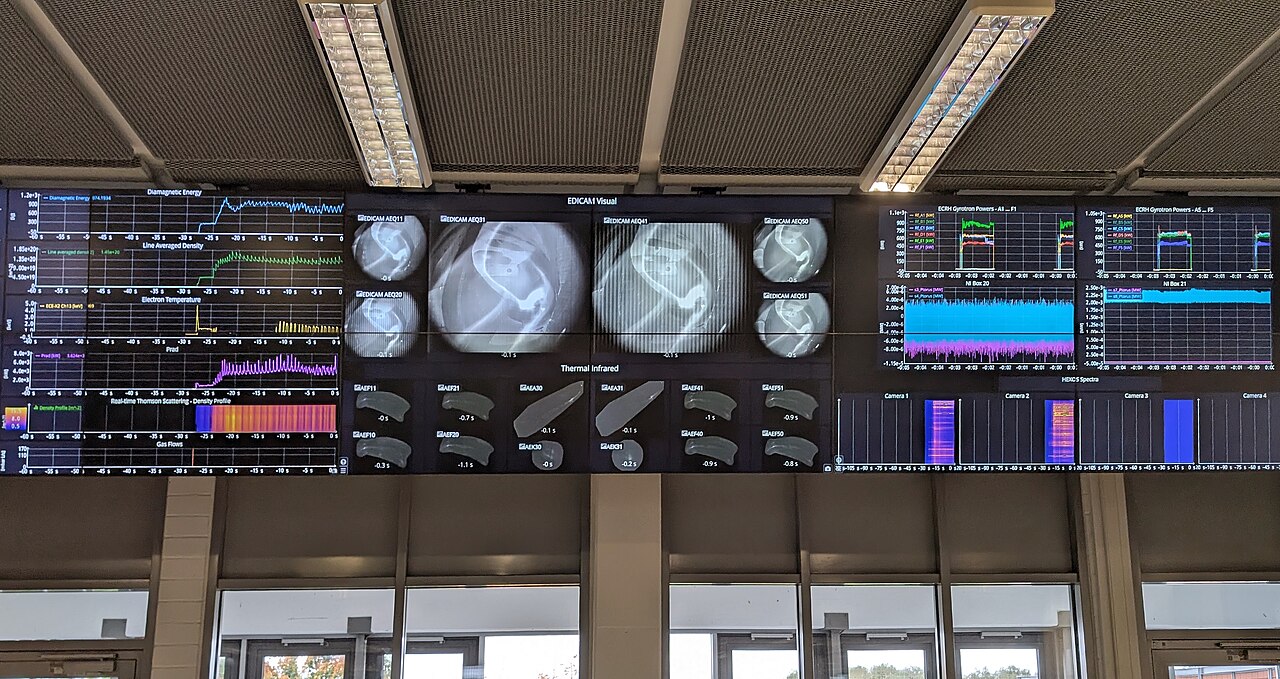 Control room with multiple monitors displaying system status panels and operational dashboards